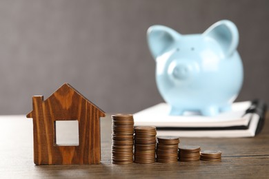 House model, stacked coins, piggy bank and notebook on wooden table, selective focus