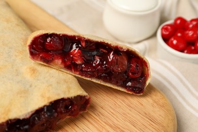 Photo of Delicious strudel with cherries on wooden board, closeup