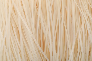 Raw rice noodles as background, closeup. Delicious pasta