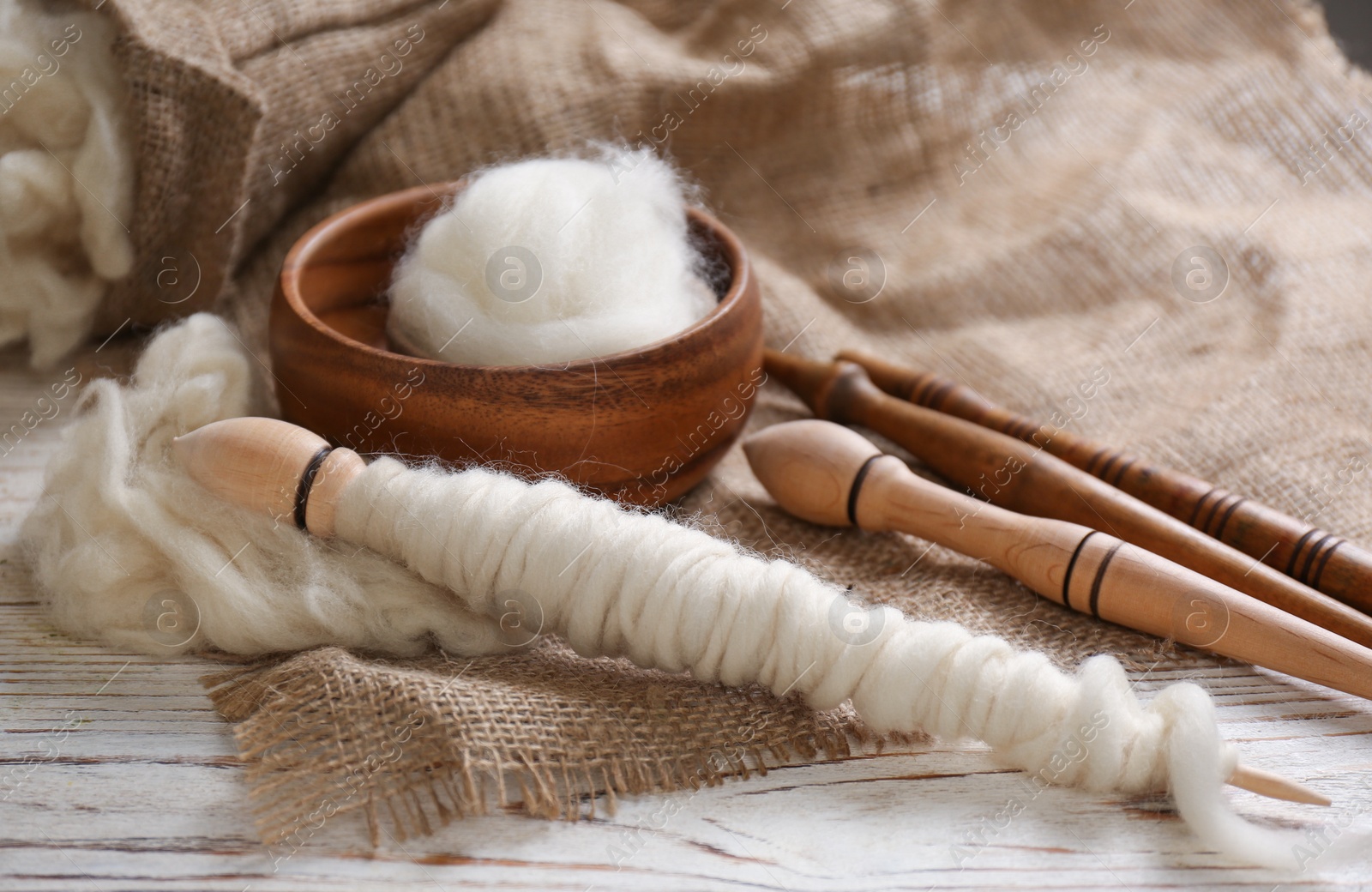 Photo of Soft white wool and spindles on wooden table, closeup