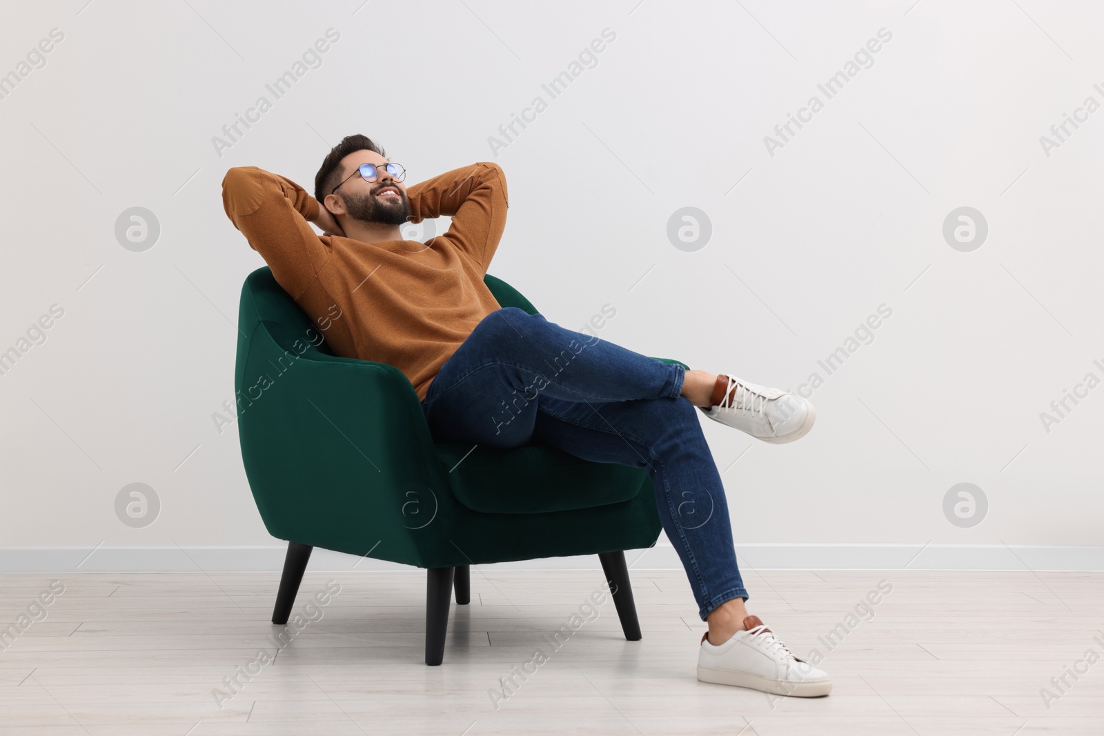 Photo of Handsome man relaxing in armchair near white wall indoors