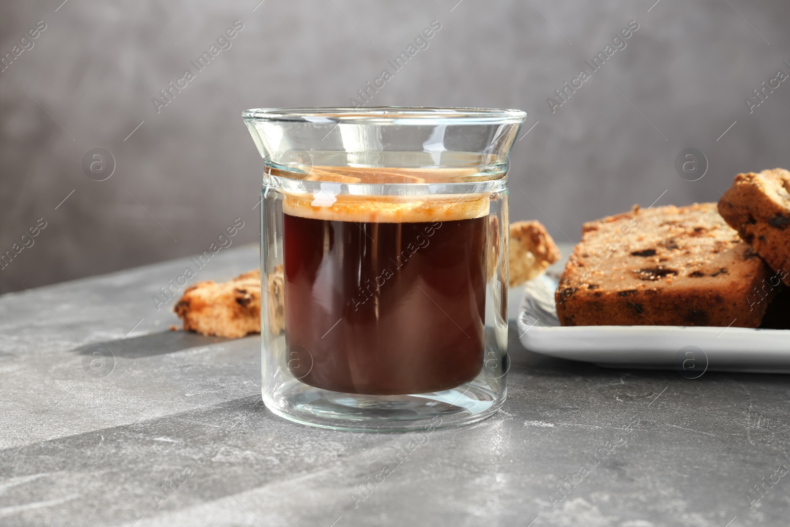 Photo of Glass of delicious coffee and plate with cake on grey table