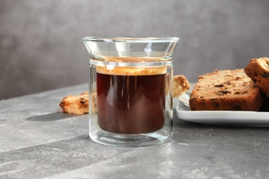 Glass of delicious coffee and plate with cake on grey table