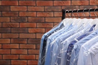 Photo of Dry-cleaning service. Many different clothes in plastic bags hanging on rack against brick wall, space for text