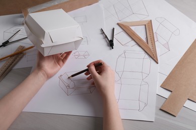 Woman creating packaging design at light wooden table, closeup