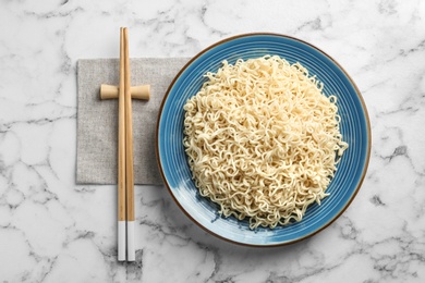 Photo of Plate of tasty noodles and chopsticks served on marble table, flat lay