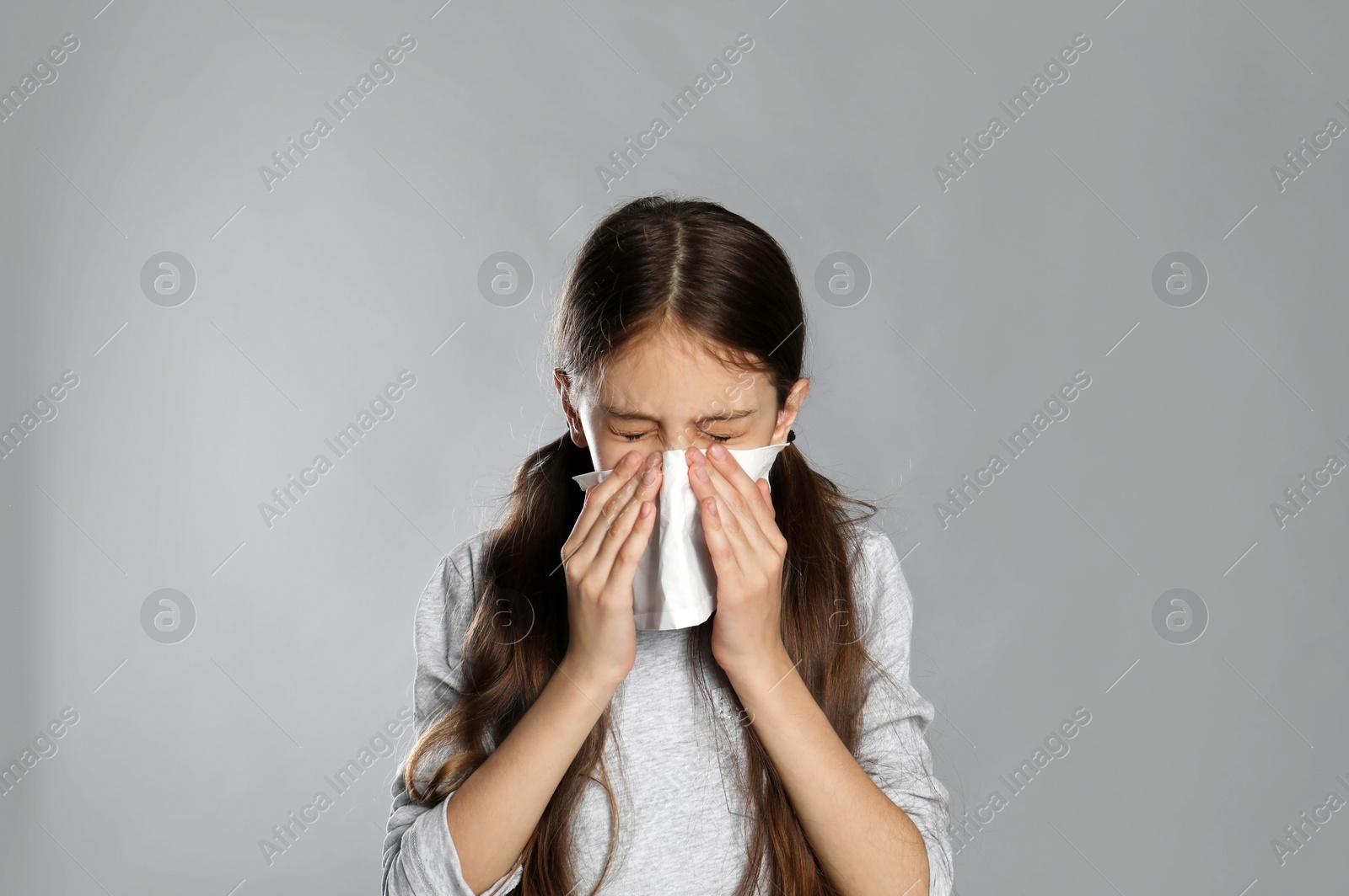 Photo of Little girl blowing nose into paper tissue on light grey background. Seasonal allergy