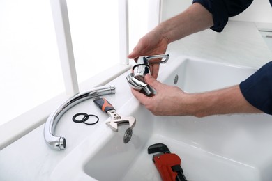 Photo of Professional plumber fixing water tap in kitchen, closeup