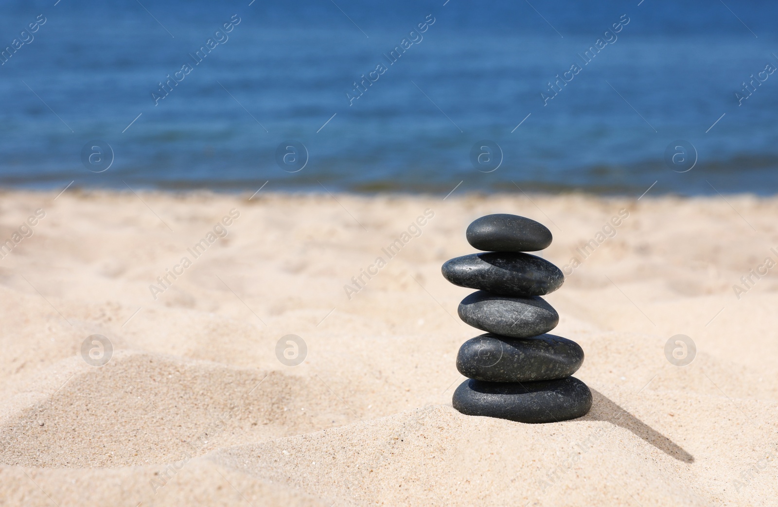 Photo of Stack of stones on sand near sea, space for text. Zen concept