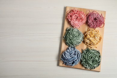 Photo of Rolled pasta painted with food colorings on white wooden table, top view. Space for text