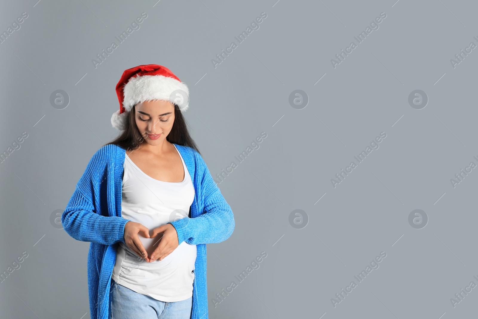 Photo of Happy pregnant woman wearing Santa hat for Christmas party on grey background, space for text. Expecting baby