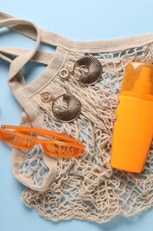 Photo of String bag, sunscreen, sunglasses and earrings on light blue background, top view