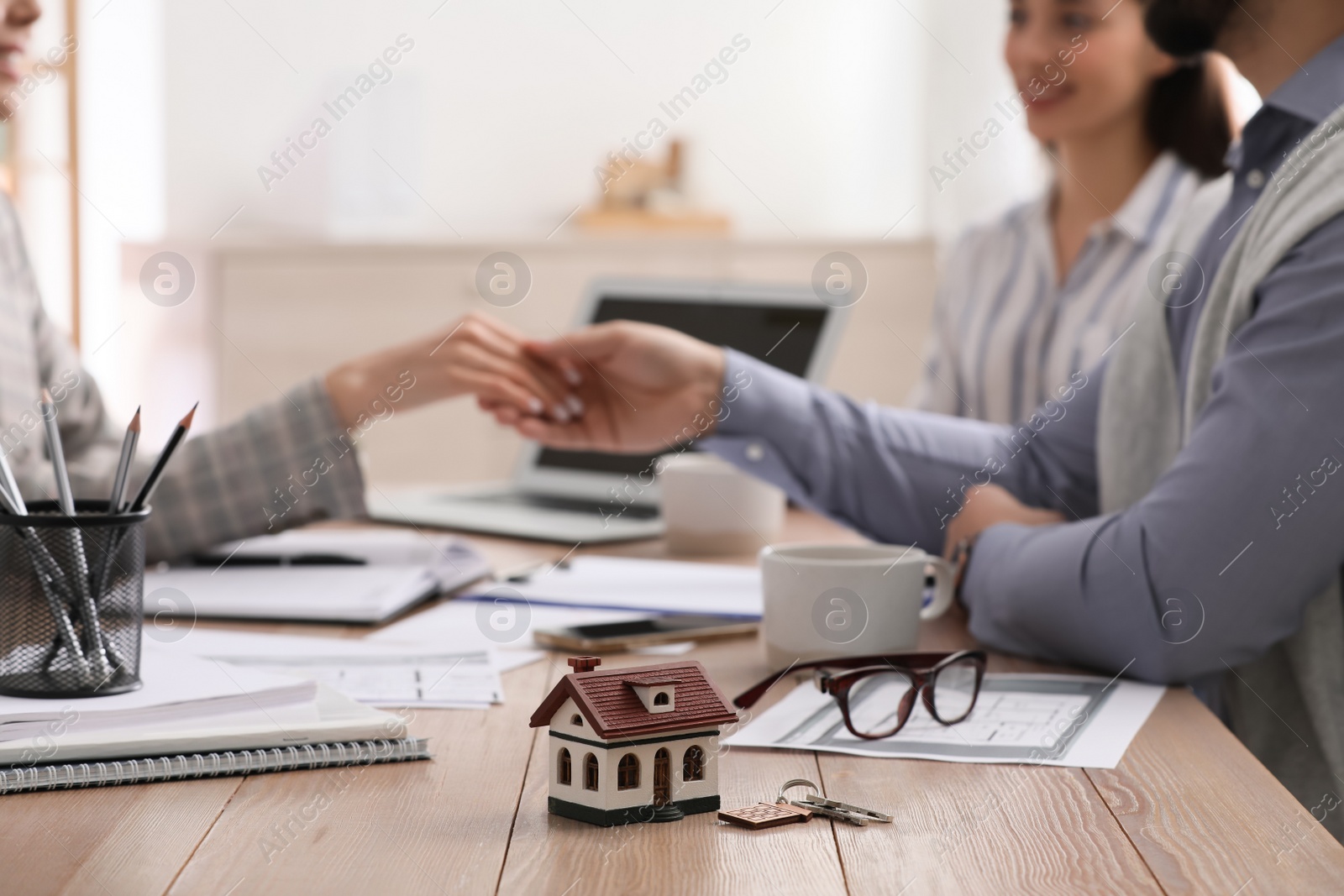 Photo of Real estate agent shaking hands with client in office, focus on house model and key. Mortgage concept