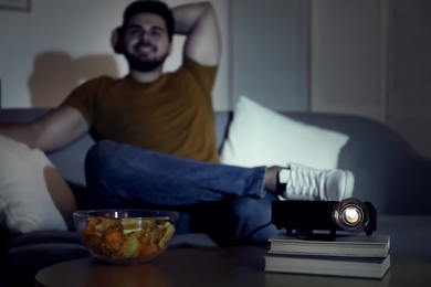 Photo of Young man watching movie at home, focus on video projector. Space for text