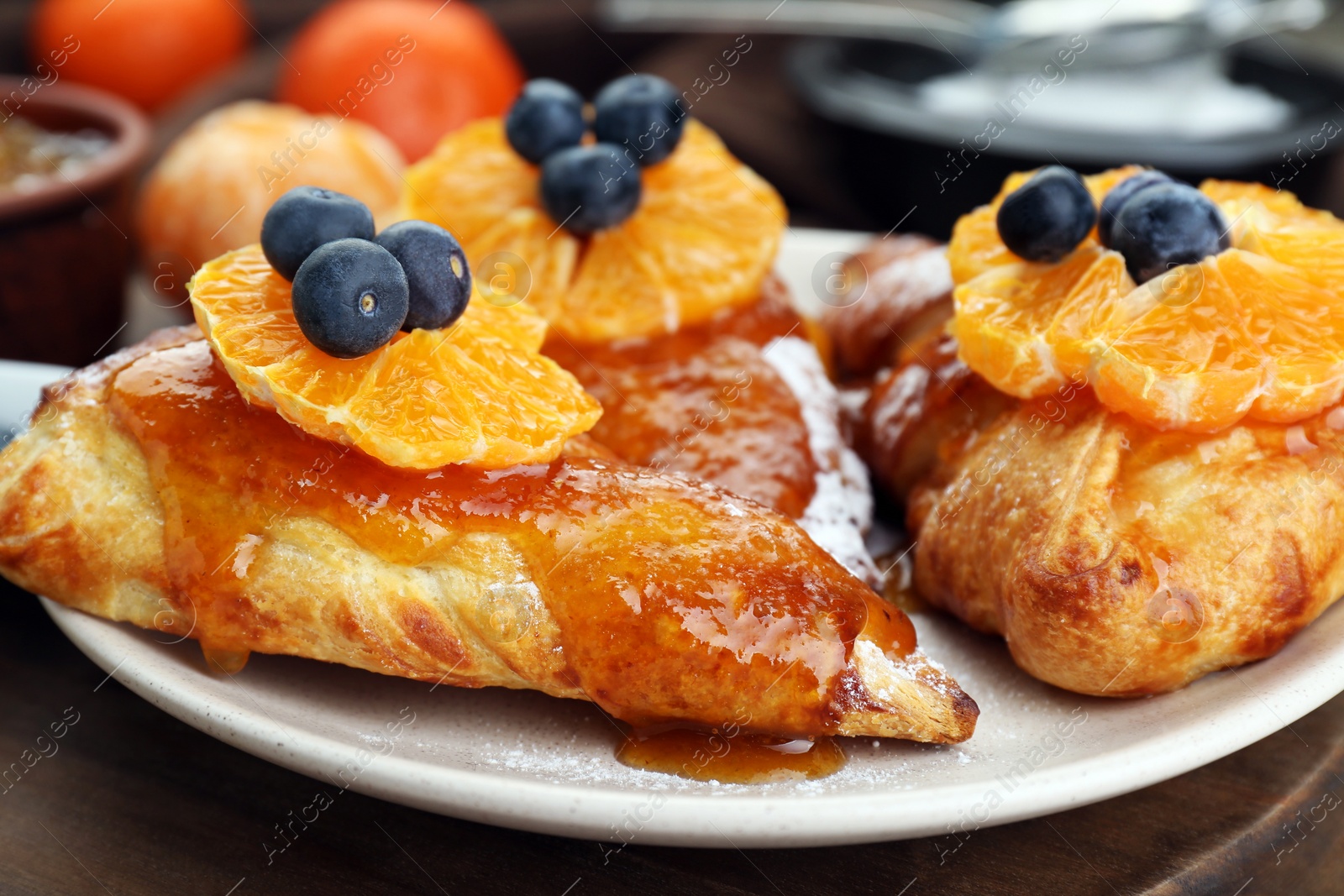 Photo of Fresh tasty puff pastry with sugar powder, jam, tangerines and blueberries on wooden table, closeup