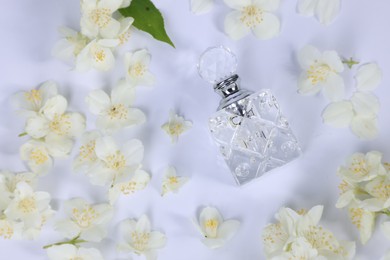 Photo of Aromatic perfume in bottle and beautiful jasmine flowers on white background, flat lay