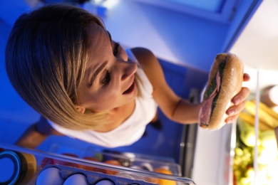 Photo of Woman taking sandwich out of refrigerator in kitchen at night, high angle view