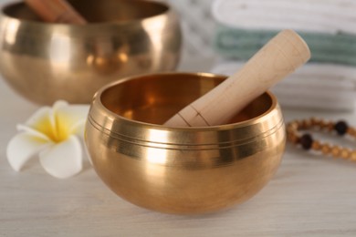 Photo of Golden singing bowl with mallet on white wooden table, closeup
