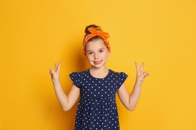 Photo of Cute little girl wearing stylish bandana on orange background