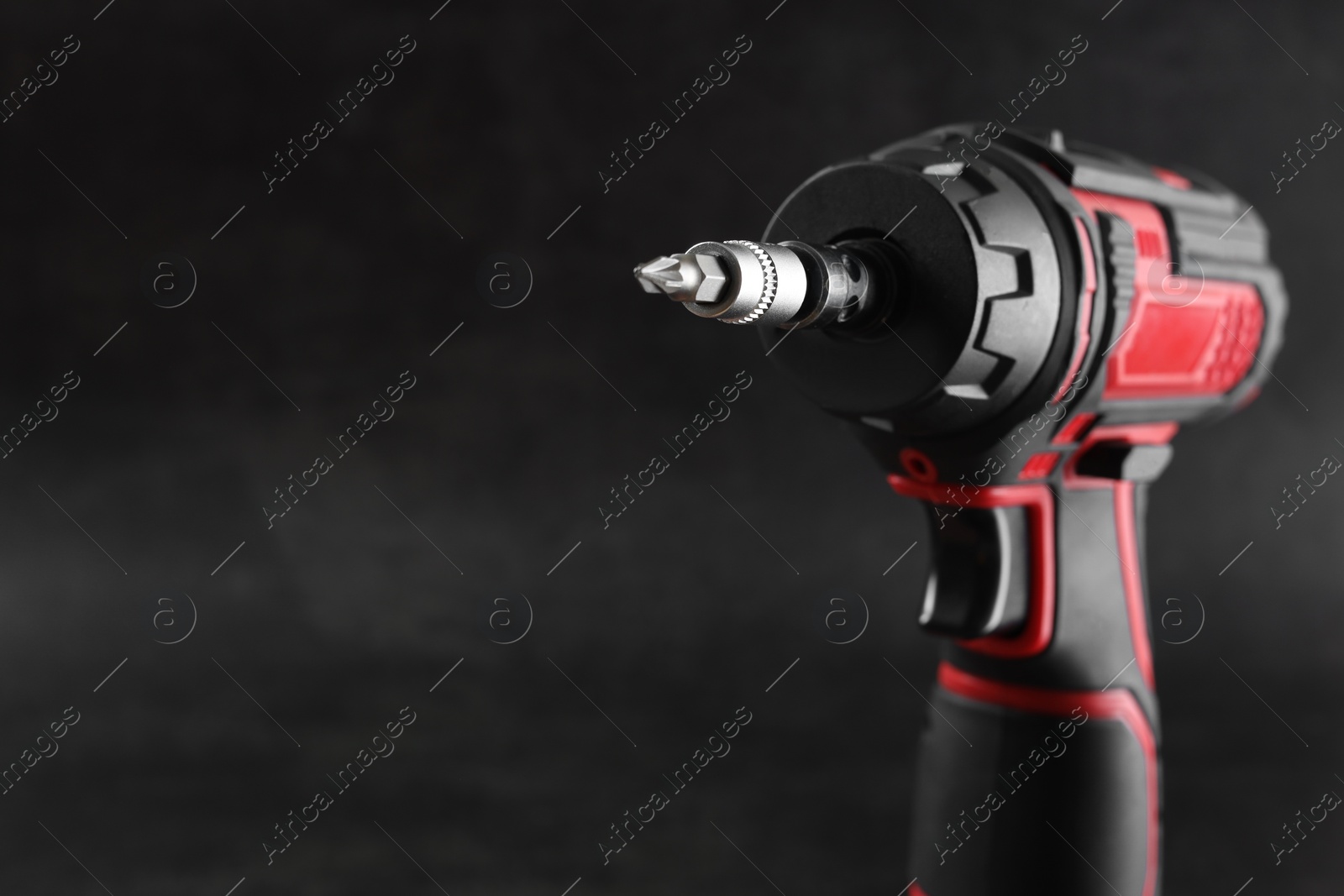 Photo of Modern electric screwdriver on dark grey background, closeup. Space for text