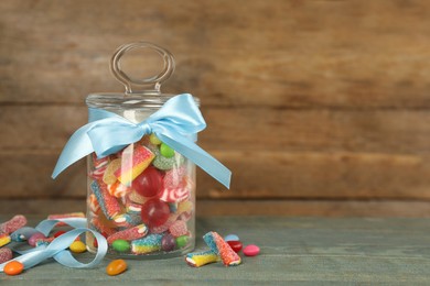 Jar with different delicious candies on light blue wooden table, space for text