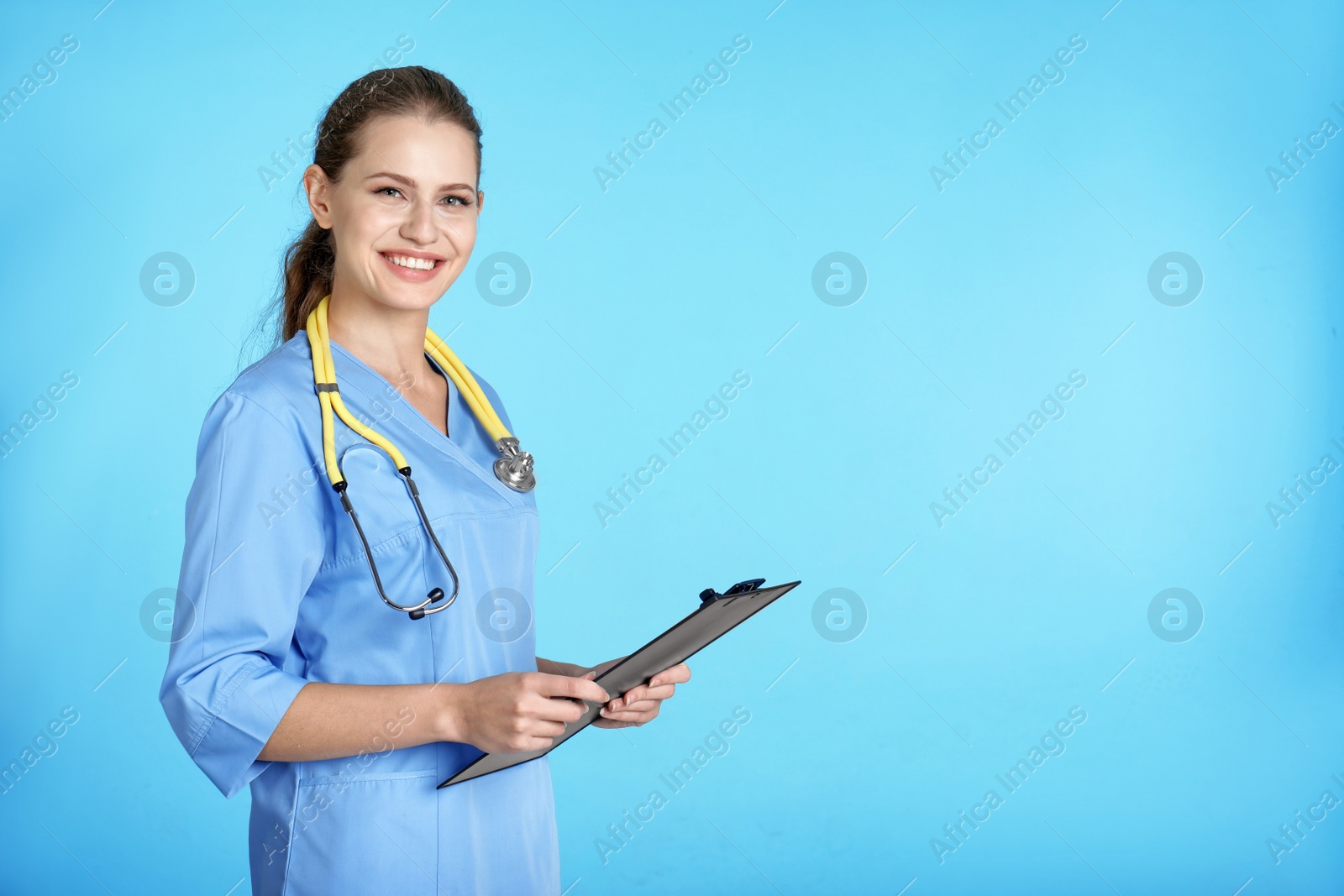 Photo of Portrait of young medical assistant with stethoscope and clipboard on color background. Space for text