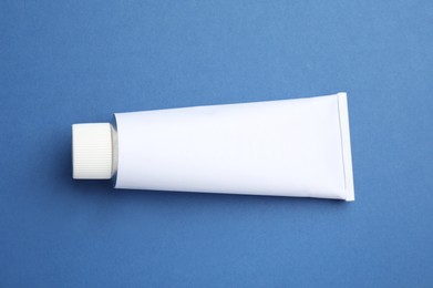 Photo of Blank white tube of ointment on blue background, top view. Space for text