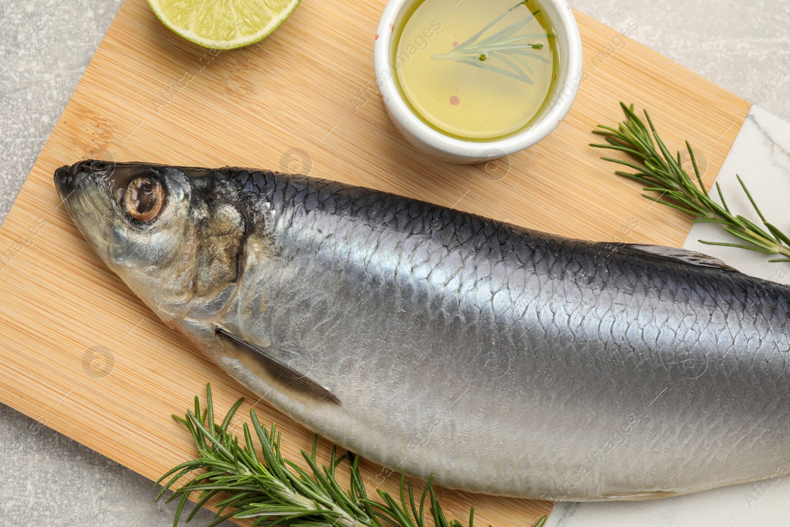 Photo of Wooden board with salted herring, lime, oil and rosemary on grey table, top view