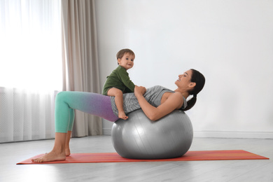 Photo of Young woman doing exercise with her son indoors. Home fitness