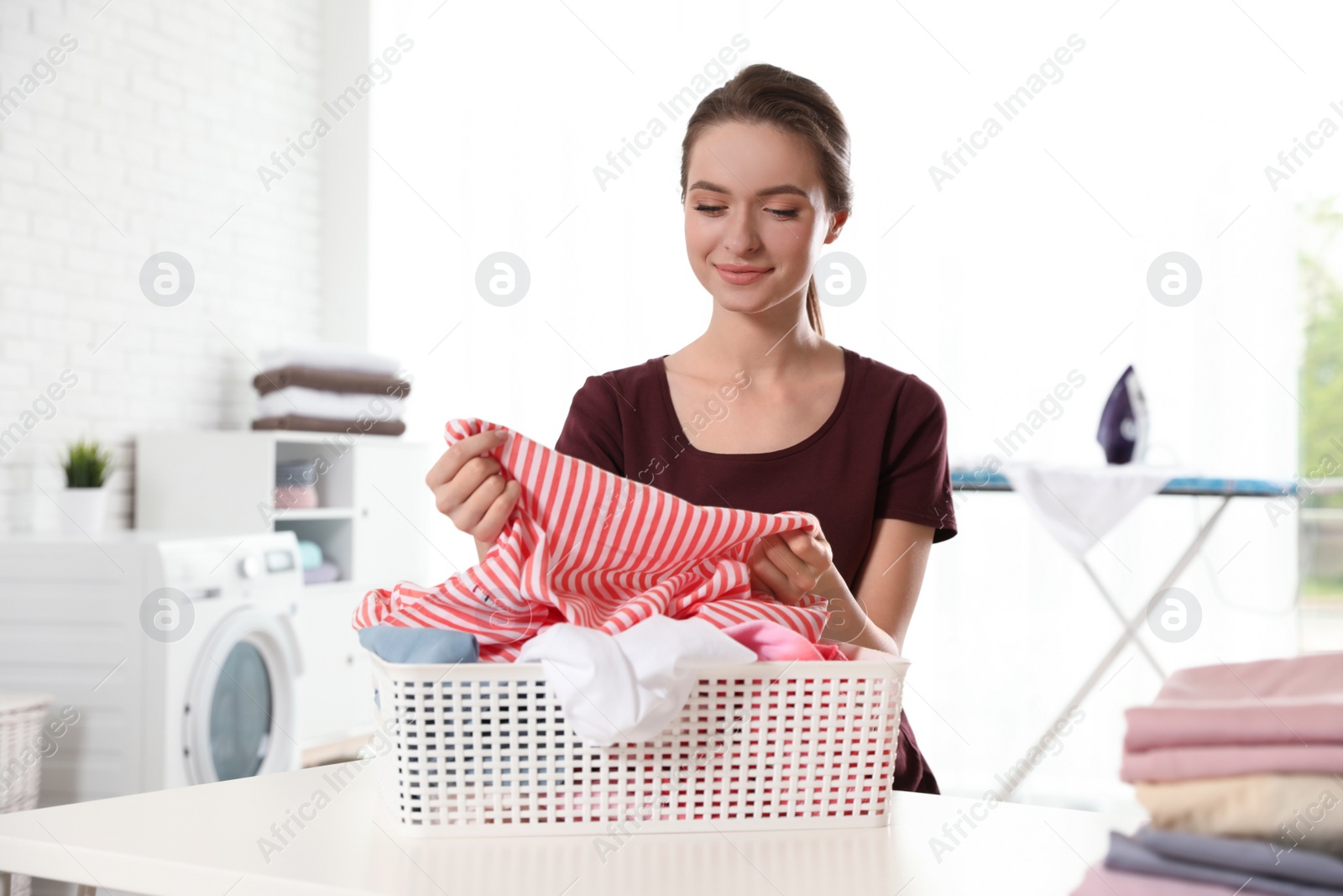 Photo of Happy woman with clean laundry at table indoors