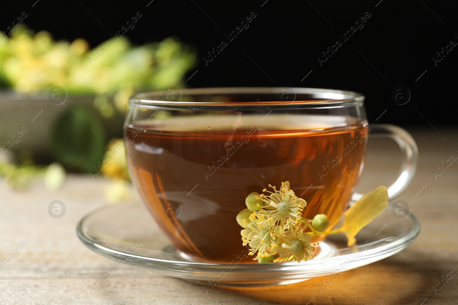 Photo of Cup of tea and linden blossom on wooden table, closeup