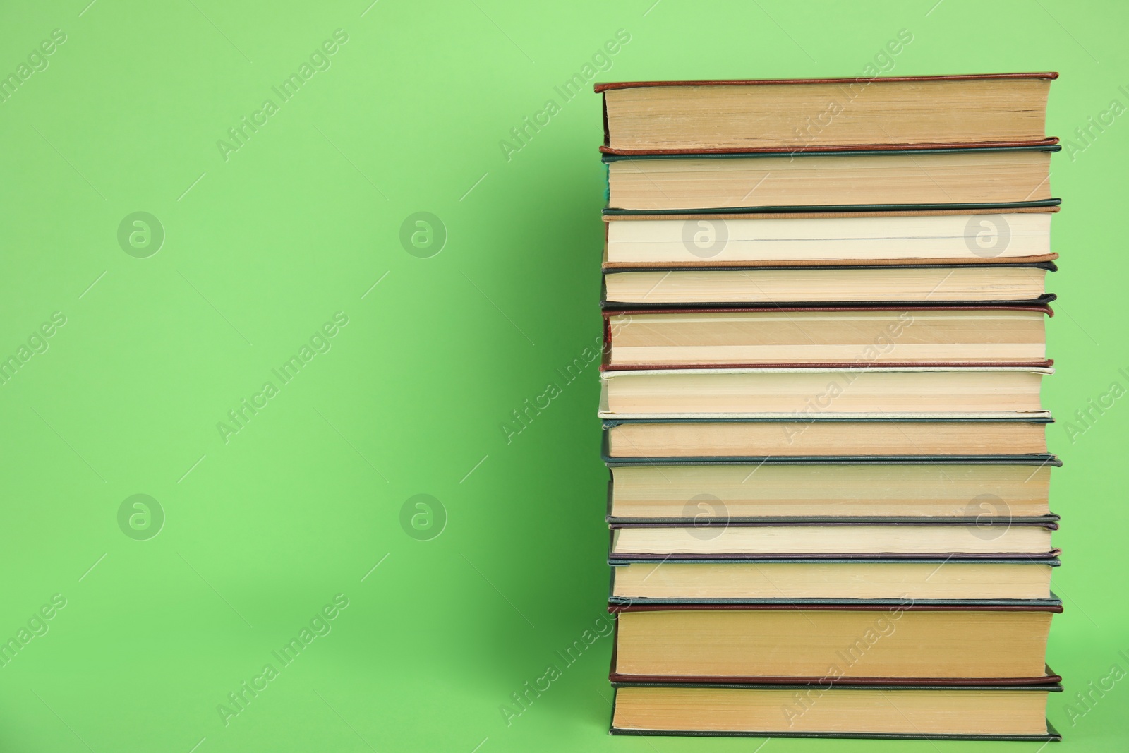 Photo of Stack of hardcover books on green background. Space for text