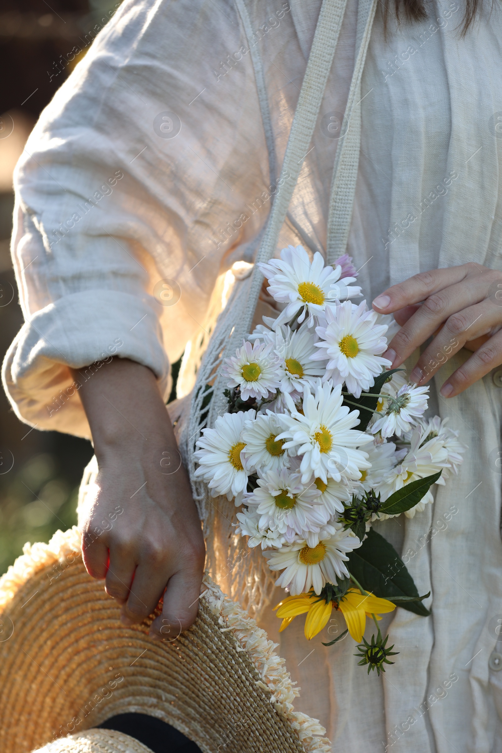 Photo of Woman holding net bag of beautiful white chamomile flowers outdoors, closeup