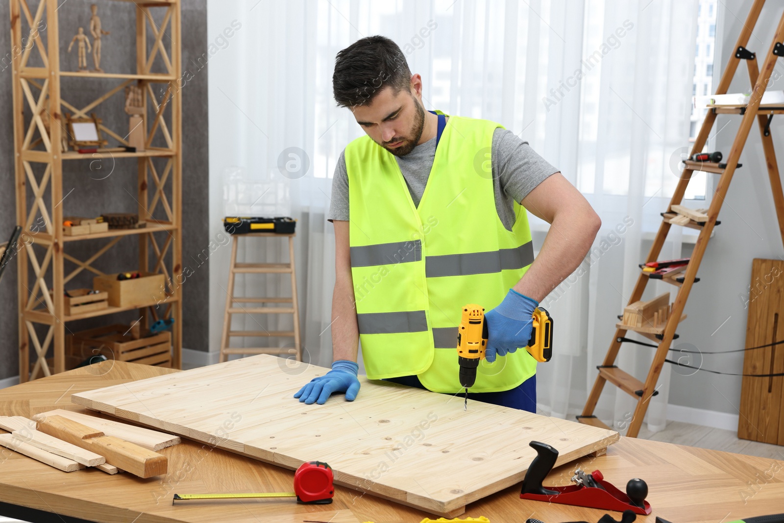 Photo of Young worker using electric drill at table in workshop