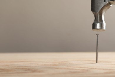 Photo of Hammering metal nail on wooden table against grey background, closeup. Space for text