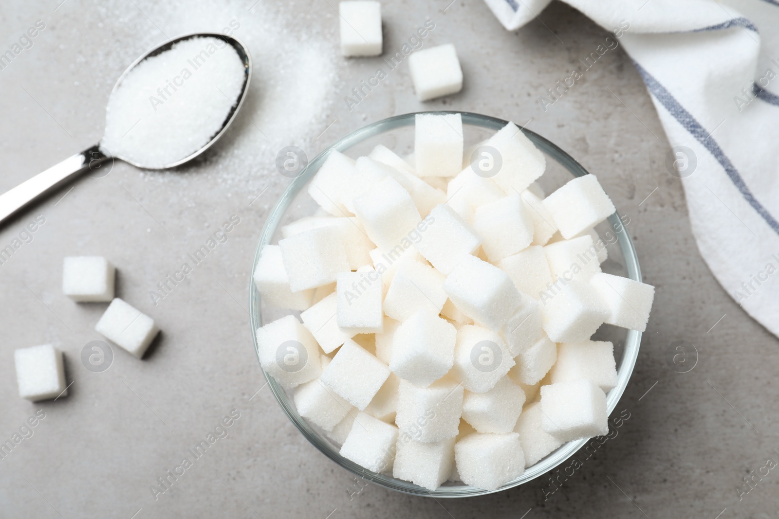 Photo of Refined sugar in bowl and spoon on grey table, flat lay