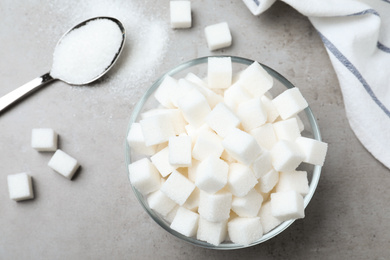 Photo of Refined sugar in bowl and spoon on grey table, flat lay