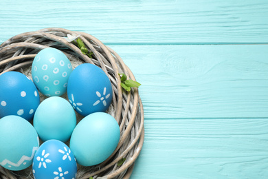 Nest with Easter eggs on light blue wooden background, top view. Space for text