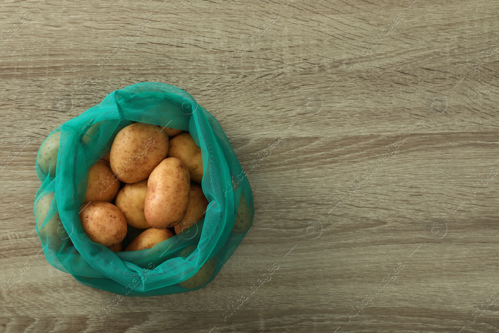 Photo of Net bag with potatoes on wooden table, top view. Space for text