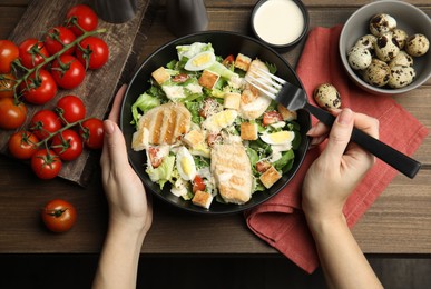 Photo of Woman eating delicious Caesar salad at wooden table, top view