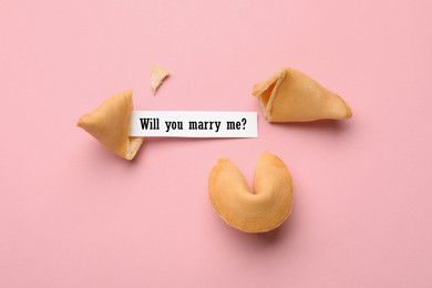 Image of Tasty fortune cookies and paper with phrase Will you marry me? on pink background, above view