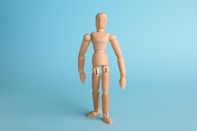 Photo of Wooden human model on light blue background. Mini mannequin