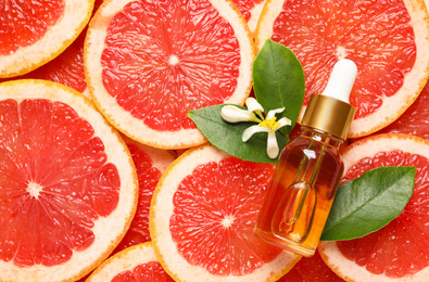 Photo of Bottle of citrus essential oil and flower on pile of grapefruit slices, flat lay. Space for text