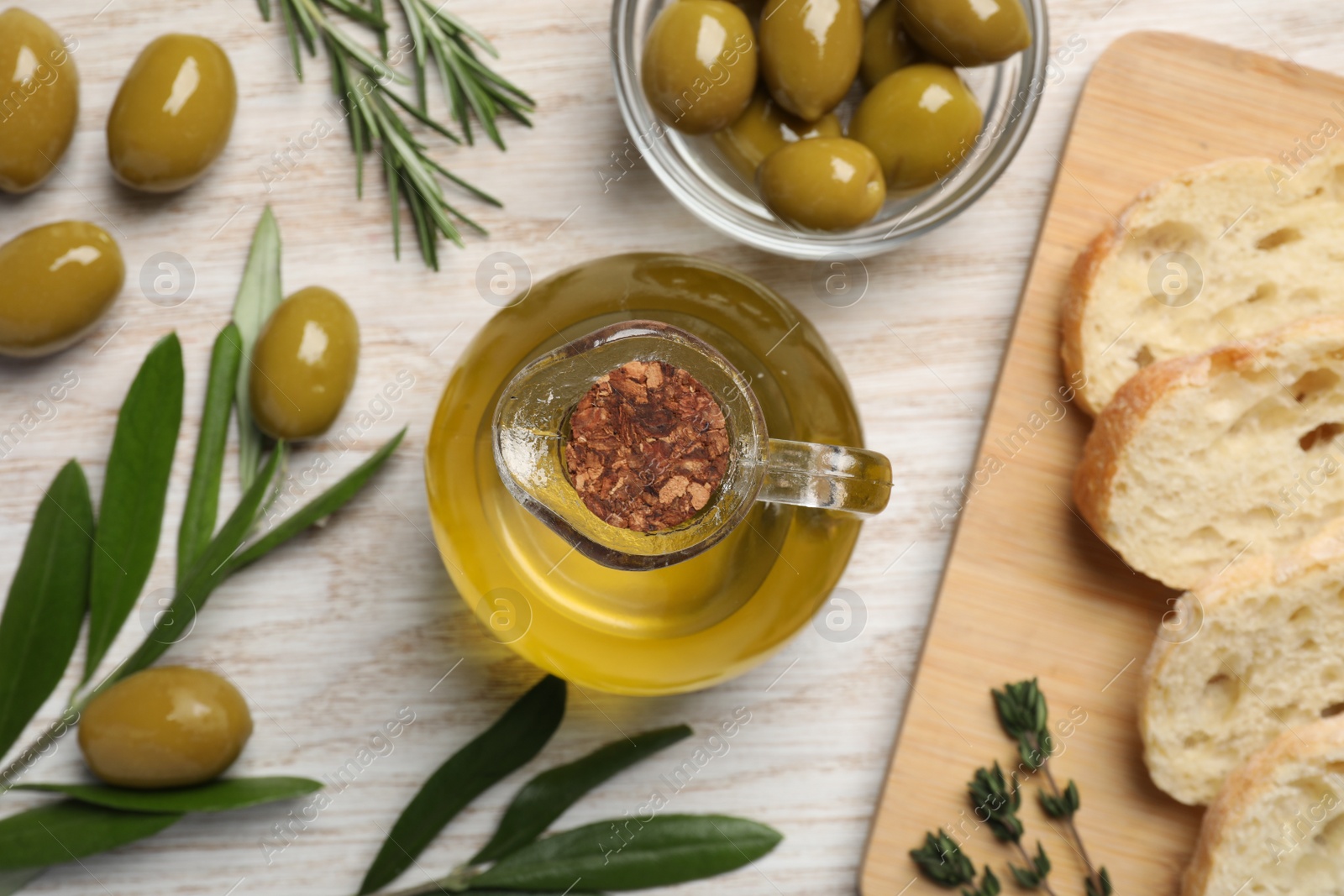 Photo of Cooking oil in jug, olives, herbs and ciabatta bread on wooden table, flat lay