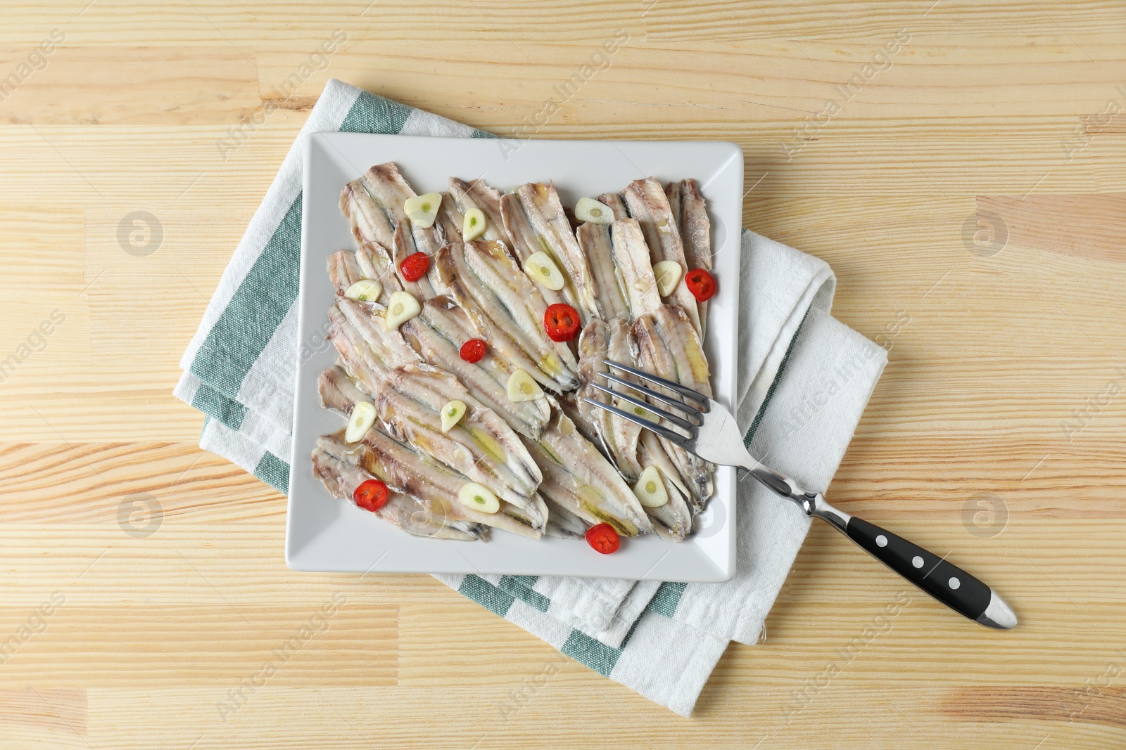 Photo of Tasty pickled anchovies with garlic, chili pepper and fork on wooden table, top view