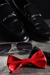 Photo of Stylish red and black bow ties, sunglasses and shoes on gray textured background