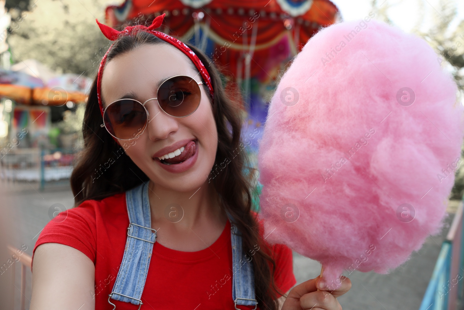 Photo of Stylish young woman with cotton candy taking selfie at funfair