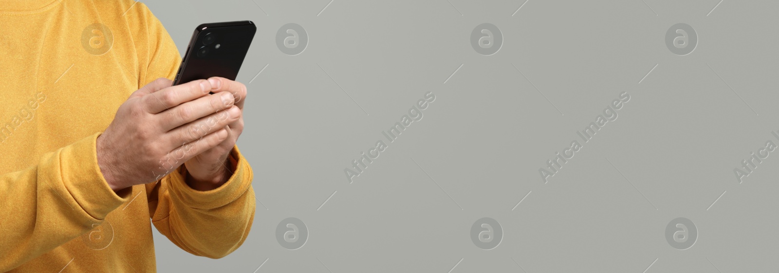 Image of Man typing message on mobile phone against grey background, closeup. Banner design with space for text