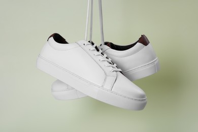 Pair of stylish sports shoes hanging on beige background