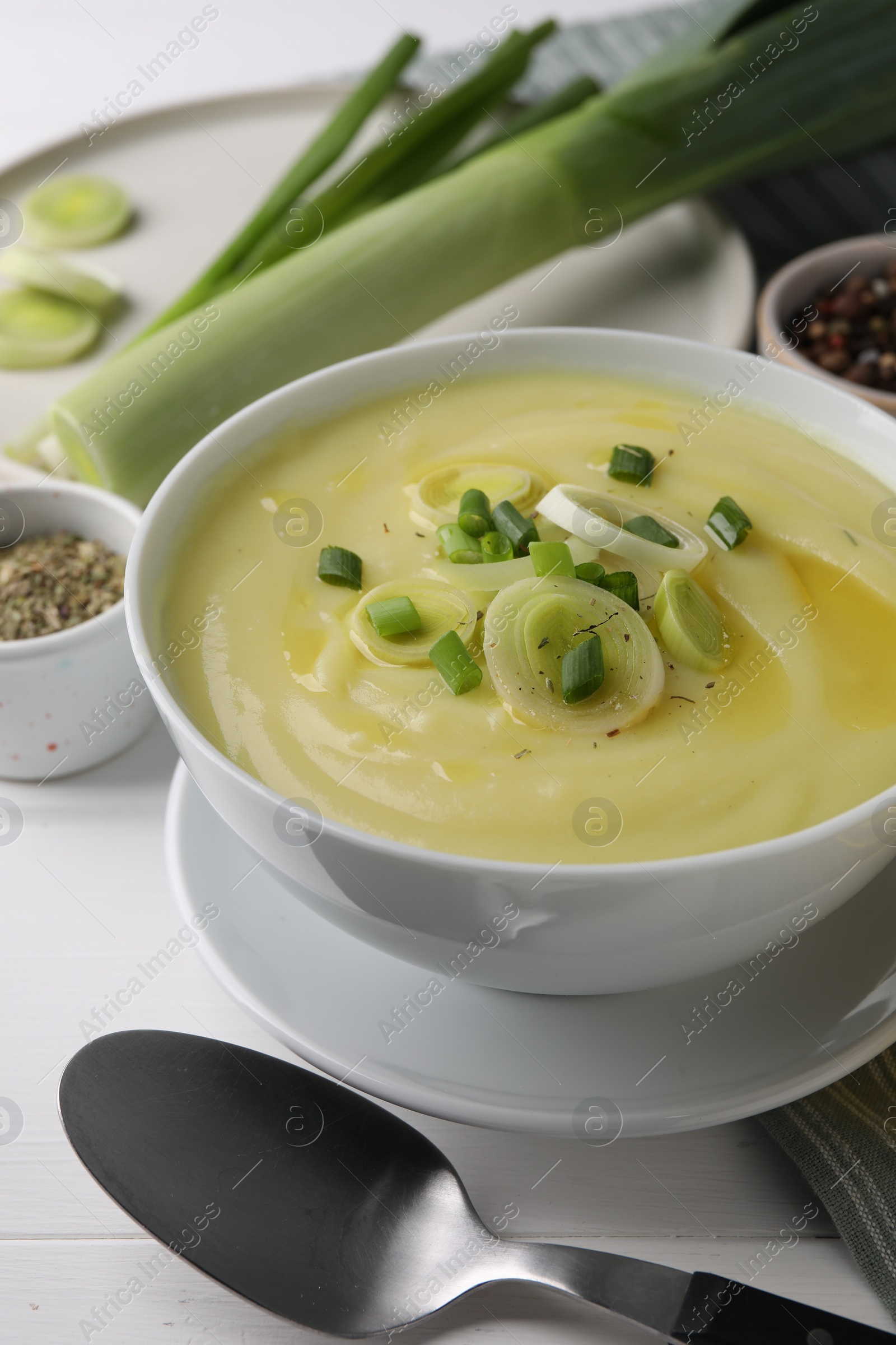 Photo of Bowl of tasty cream soup with leek and spoon on white wooden table